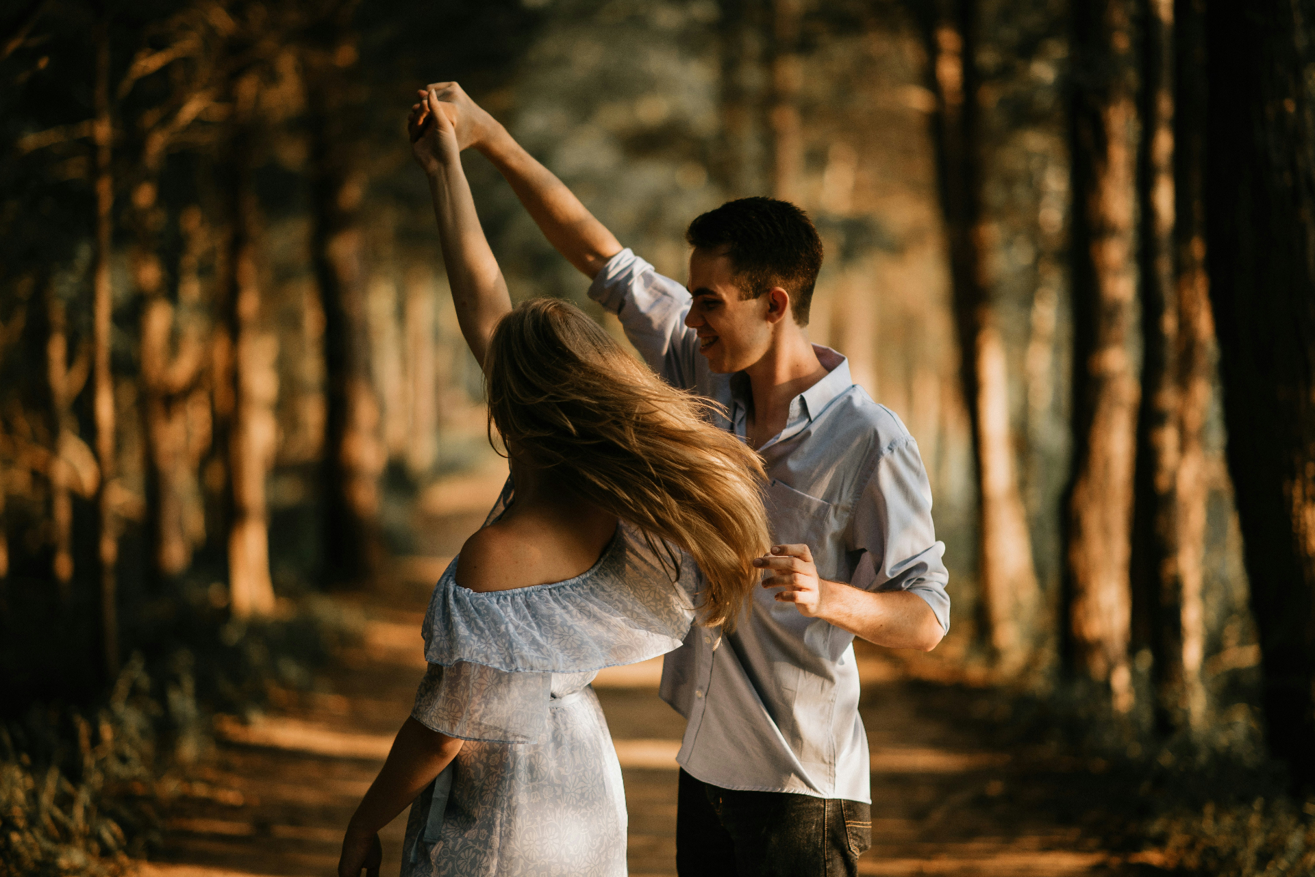 A couple dancing and twirling on a sunlit forest path, moving through a new, playful pattern together.